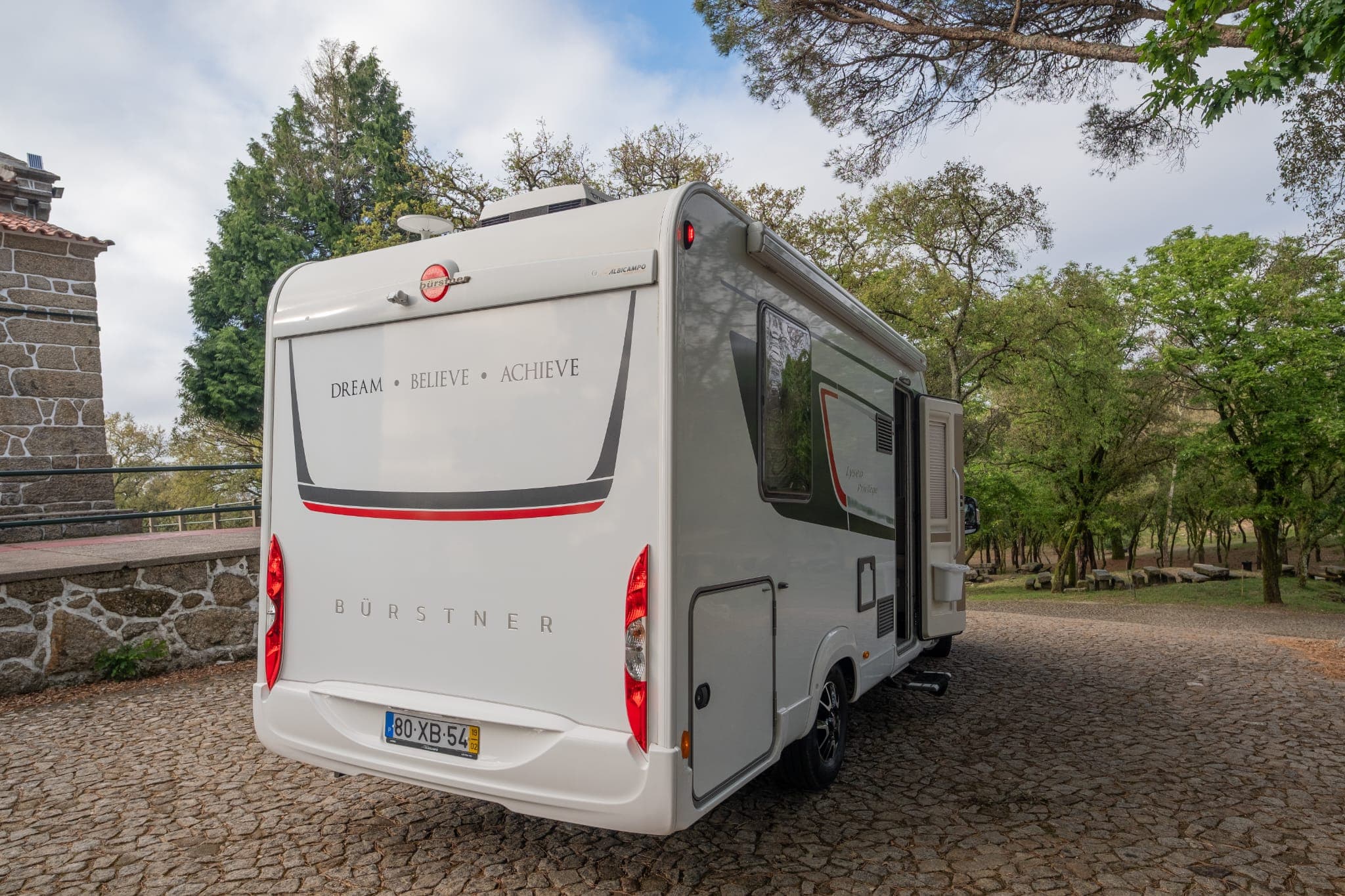 Traseira da autocaravana num largo empedrado rodeado de árvores